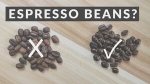 Freshly ground coffee beans beside an espresso portafilter on a modern marble countertop.