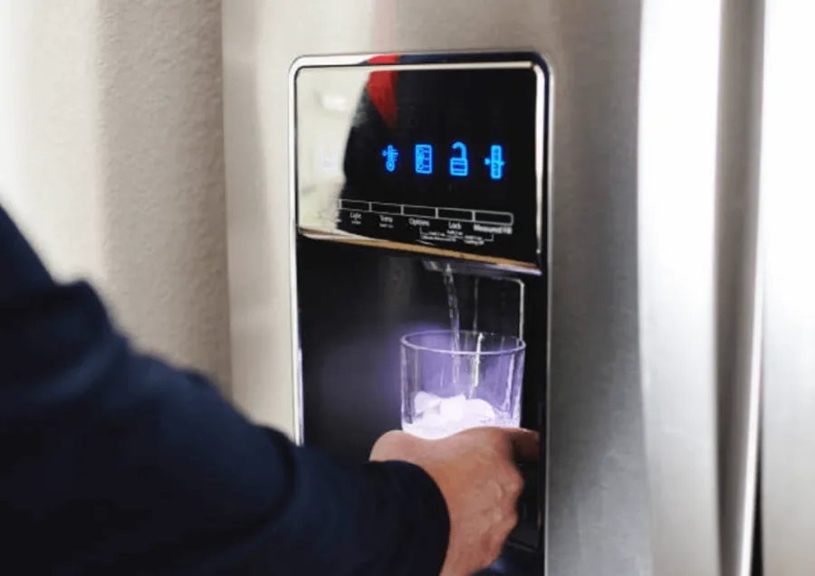 A person checking the control panel of a countertop ice maker in a kitchen.