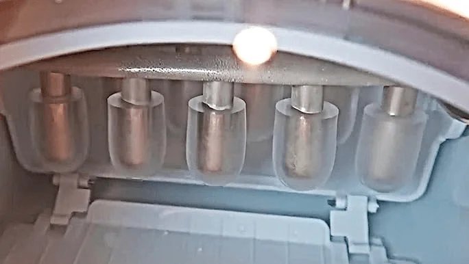 Inspecting the water inlet valve inside a refrigerator to troubleshoot ice production issues.