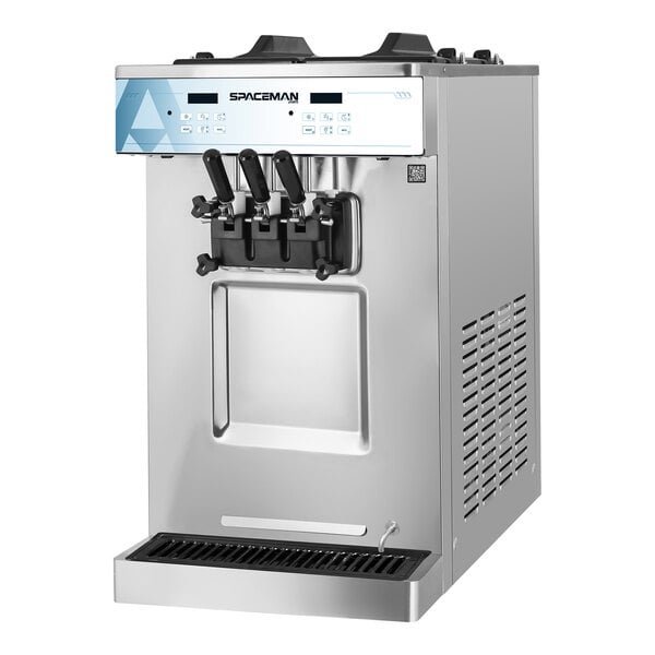 A commercial ice cream machine on a stainless steel table with planning documents nearby.