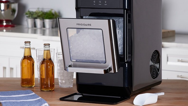 A modern countertop ice maker sits on a kitchen island with a refreshing drink.