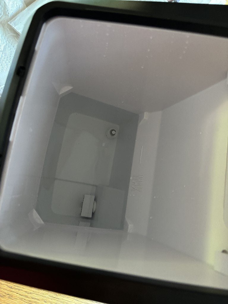 Adding water to the reservoir of a countertop ice maker for maintenance.