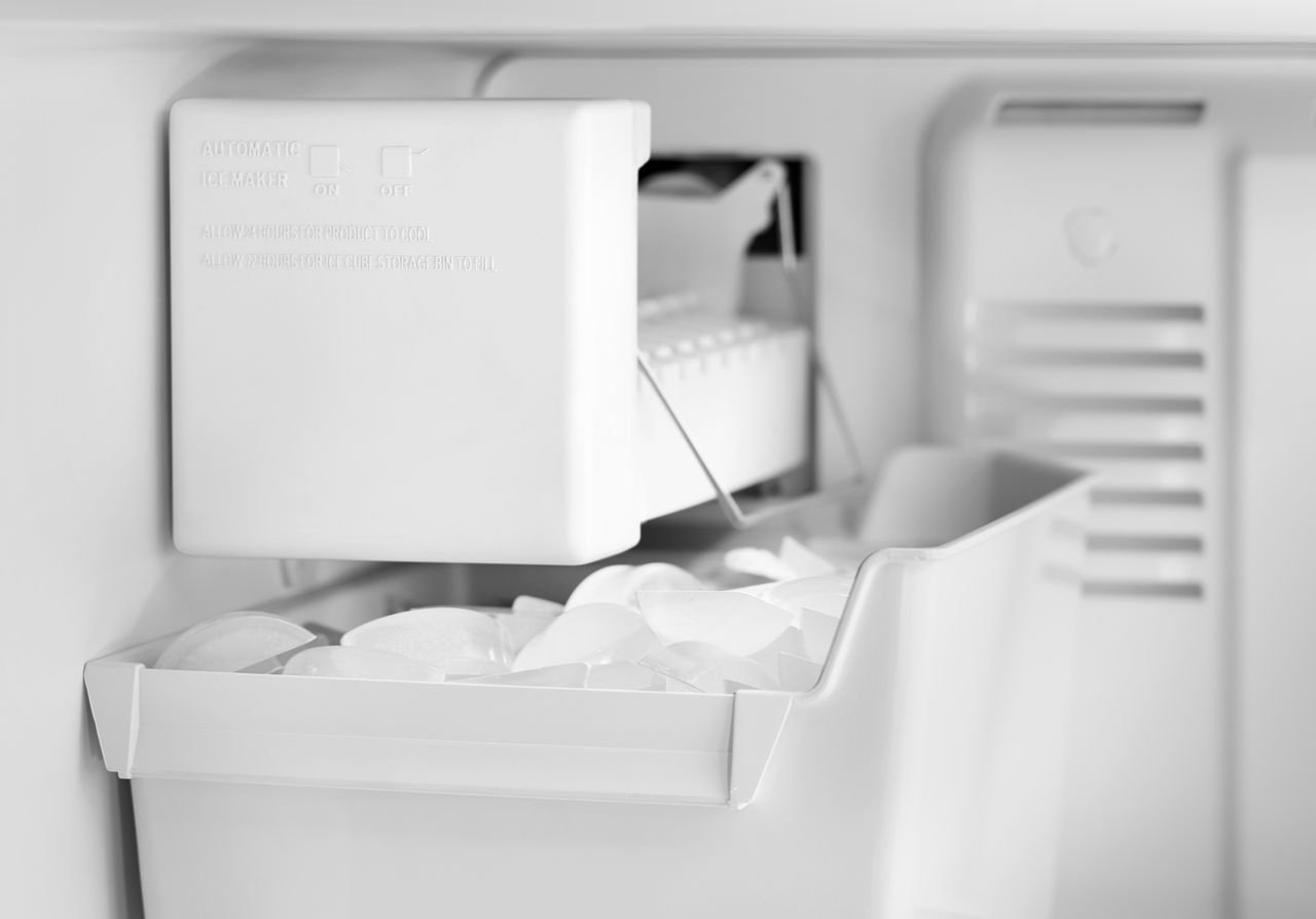 A hand lowering the metal wire arm to activate the freezer ice maker.