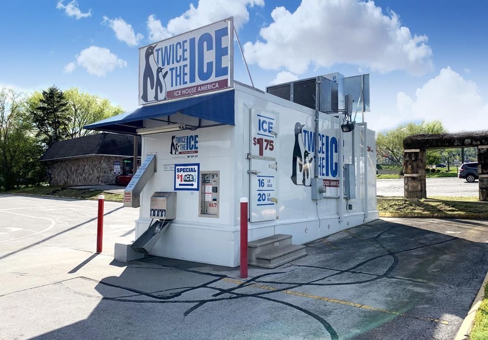 A modern ice vending machine kiosk located in a clean outdoor parking area.