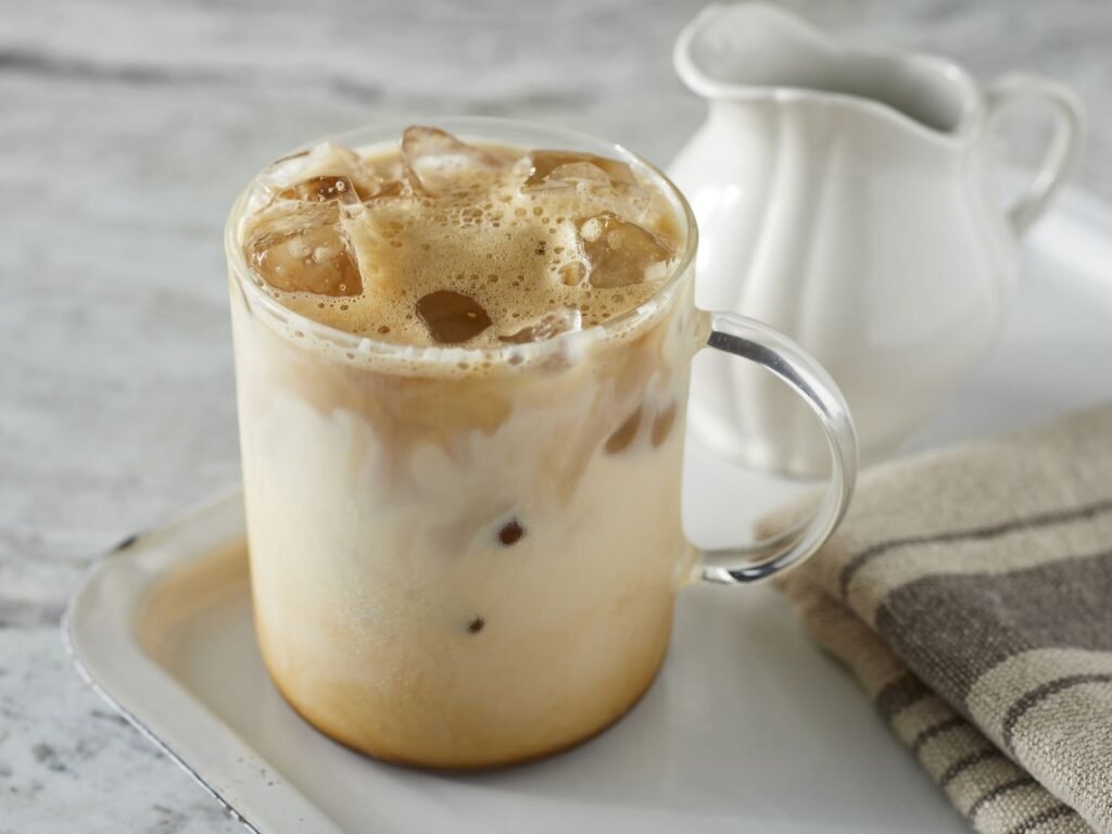 A refreshing glass of iced coffee with swirling milk on a wooden table.