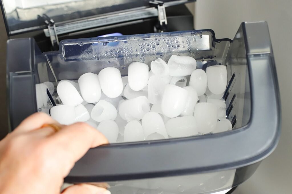 A modern stainless steel ice maker filled with fresh ice in a kitchen.