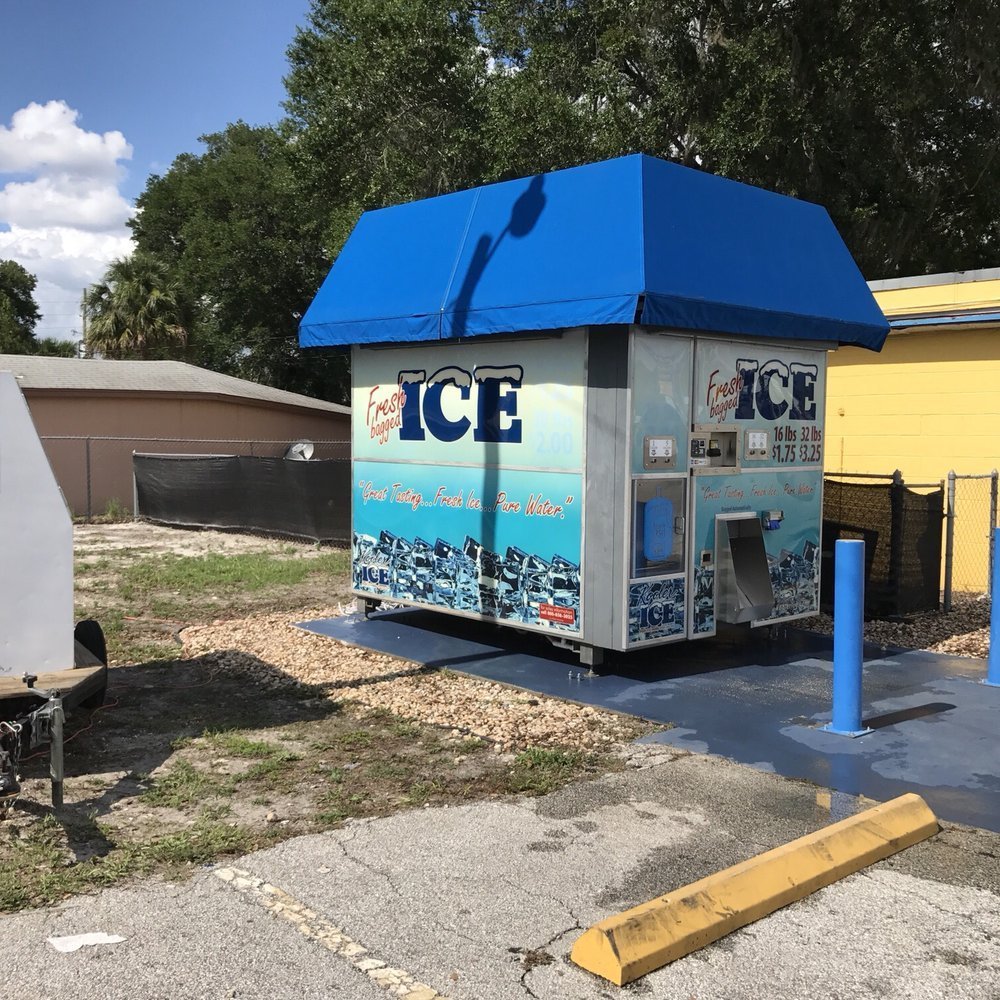 A person standing at a standalone ice machine in a suburban setting.