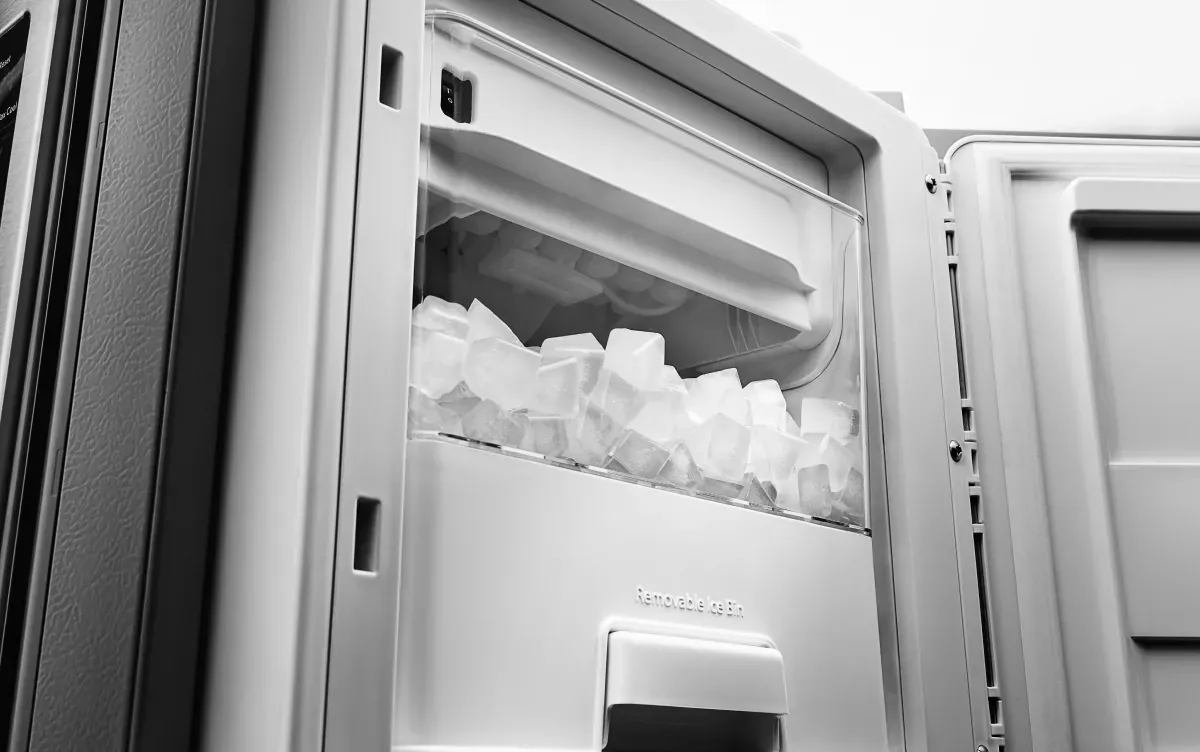 Hand checking an ice maker tray inside an open freezer compartment.