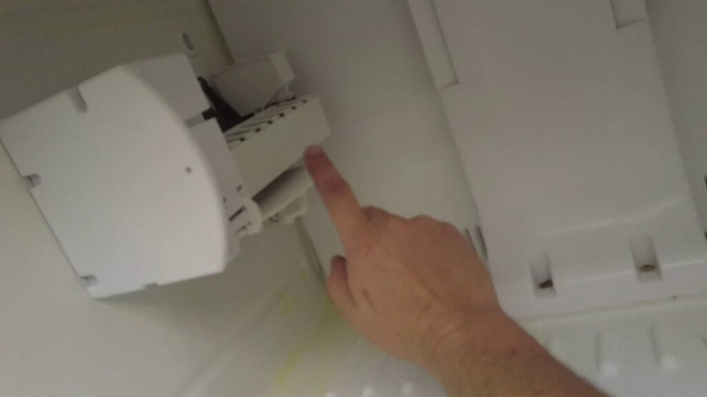Open modern kitchen freezer showing a built-in ice maker and fresh ice cubes.