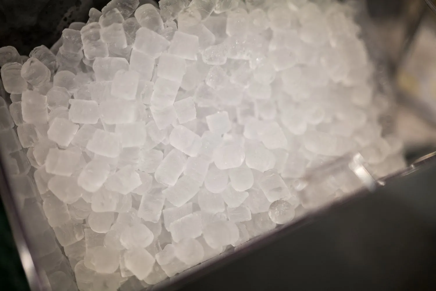 A paper cup filled with nugget ice sits near a commercial dispenser.