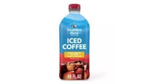 A tall glass of iced coffee next to roasted coffee beans.